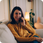 A woman lounges on a couch and speaks on a mobile phone. 